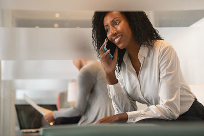 Young woman using mobile phone while sitting in laptop