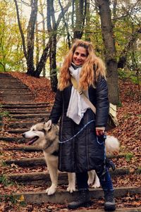 Portrait of woman standing with pet alaskan malamute on steps at forest