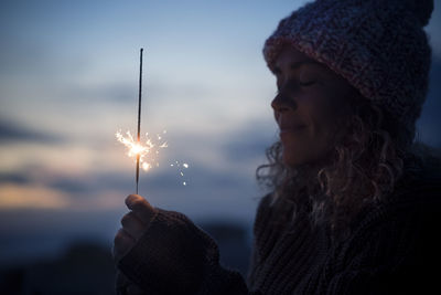 Woman holding sparkler against sky during dusk
