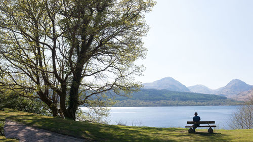 People sitting on bench by lake against sky