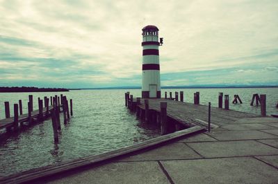 Lighthouse on pier by sea against sky