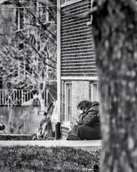 Young woman sitting by tree against building