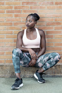 Portrait of young woman sitting against brick wall