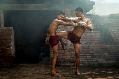 Full length of shirtless man standing against wall