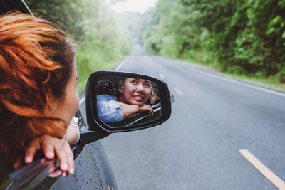 Reflection of woman in car side-view mirror on road