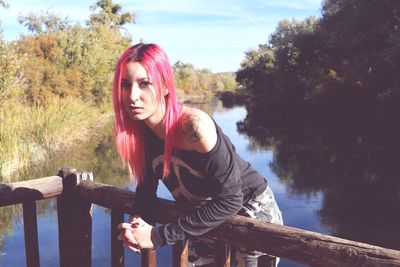 Portrait of young woman standing by railing against trees