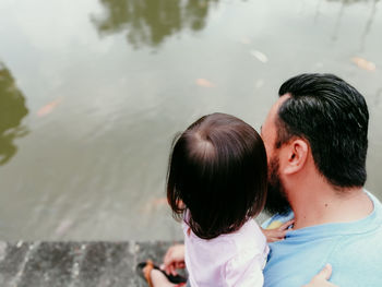 Rear view of father and daughter by lake