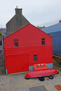 Red house on sidewalk by building against sky