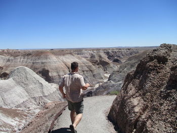 Rear view of boy walking by rock formations against clear sky