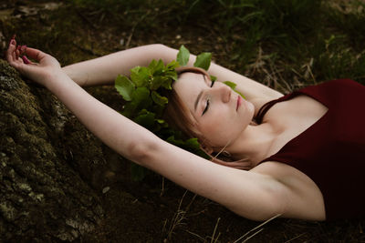 Midsection of woman young woman with closed eyes lying down on land wearing crown made of leaves 