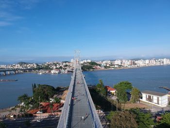 Bridge over sea by buildings against blue sky