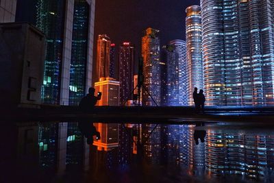 People by swimming pool against buildings in city at night