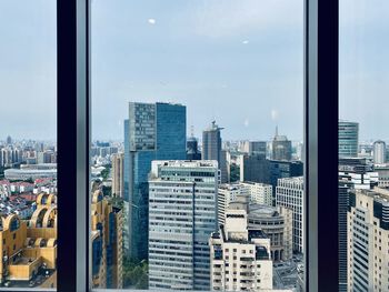 Buildings in city against sky seen through glass window