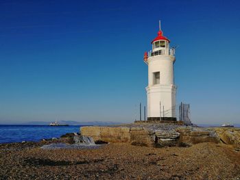 Lighthouse amidst sea and buildings against clear blue sky