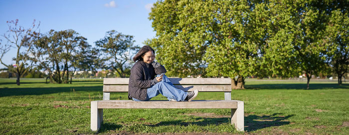 Side view of woman sitting on bench against trees