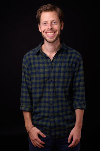 Portrait of smiling young man against black background