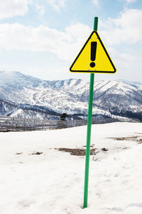 Road sign on snow covered land against sky