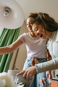 Low angle view of cheerful female friends preparing lunch in bowl at home