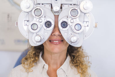 Smiling female patient examining eyesight through phoropter in medical clinic