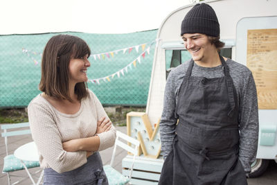 Happy male and female owners talking while standing on street outside food truck