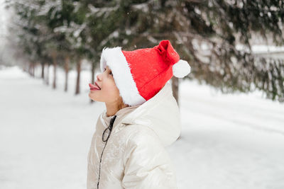 Cute girl wearing santa hat sticking out tongue during winter