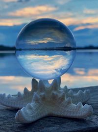 Close-up of crystal ball on beach against sky during sunset