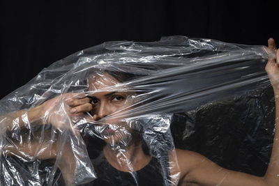 Model portrait with clear plastic in front of her face against black background. 