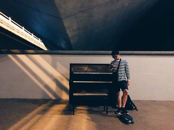 Full length of man using phone while standing with skateboard by piano