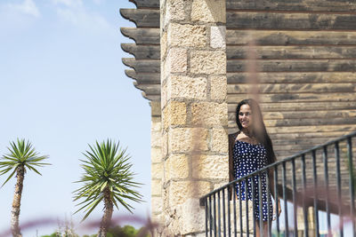 Smiling young woman standing by railing