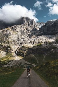 Rear view of person riding bicycle on road against mountain