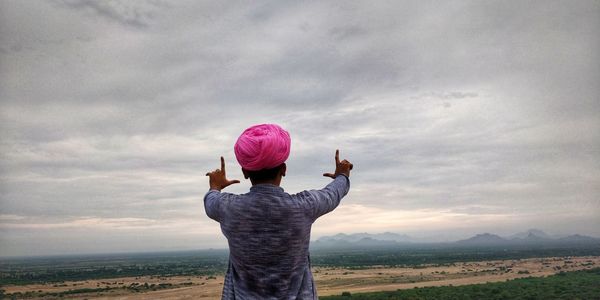 Rear view of man gesturing against sky