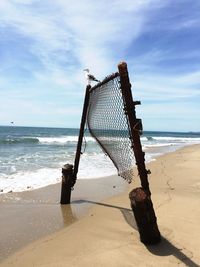 Seagull perching on broken fence at seashore against sky