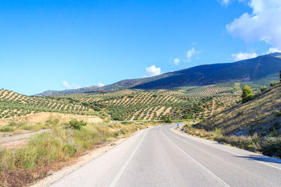 Road leading towards mountains against blue sky