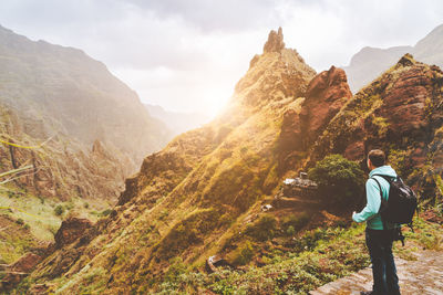 Rear view of man looking at mountains against sky