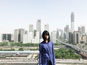 Woman standing against modern cityscape against clear sky