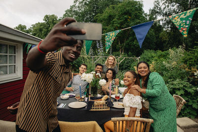 Man taking selfie with male and female friends sitting at table during party