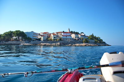 Boats in sea by buildings against clear blue sky