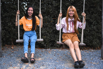Portrait of happy sisters swinging in park