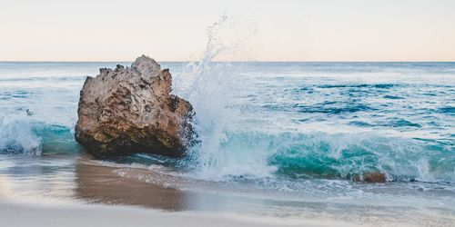 Water splashing on rock in sea against clear sky