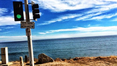 Warning sign on sea shore against blue sky
