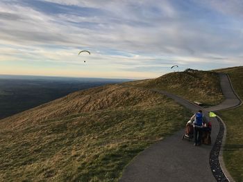 Rear view of man with baby strollers walking on road amidst fields against sky