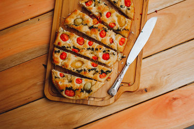 Homemade italian focaccia cut into slices, with tomato and olive oil on a rustic wooden background.