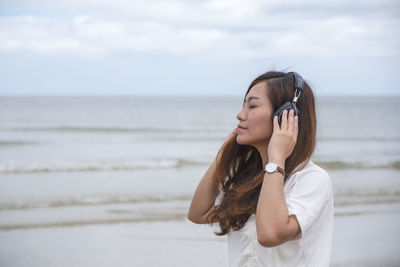 Side view of thoughtful woman wearing headphones while standing at beach
