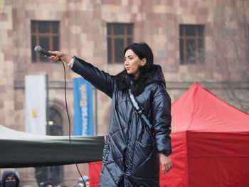 Young woman with arms outstretched standing against built structure