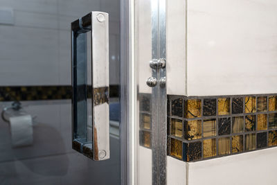 Glass door with a chrome handle in the bathroom, which is lined with decorative ceramic tiles.