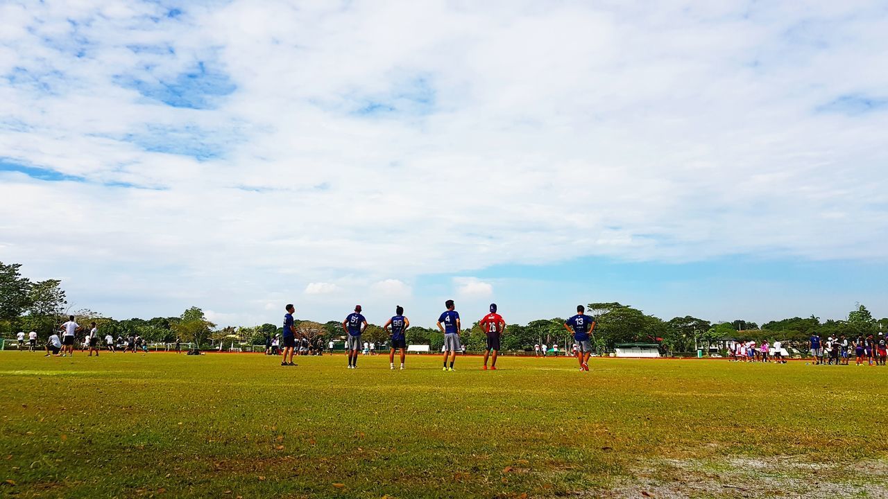 GROUP OF PEOPLE PLAYING SOCCER ON FIELD AGAINST SKY