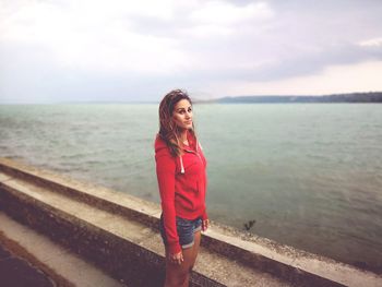 Young woman standing by sea against sky