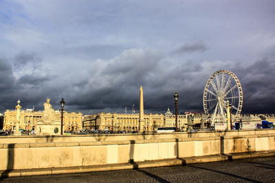 Ferris wheel in city against cloudy sky