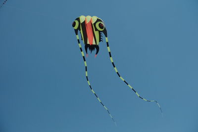 Low angle view of kites flying against clear blue sky