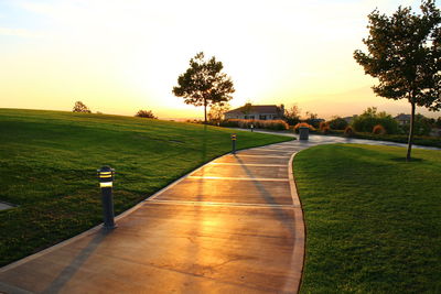 Footpath at park against sky during sunset